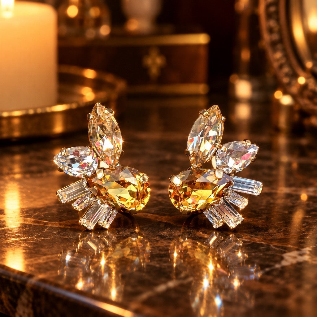 Zaria gouden oorstekers met ovale amberkleurige steen, marquise en baguette kristallen op marmeren ondergrond bij kaarslicht, DAMICE Jewelry
